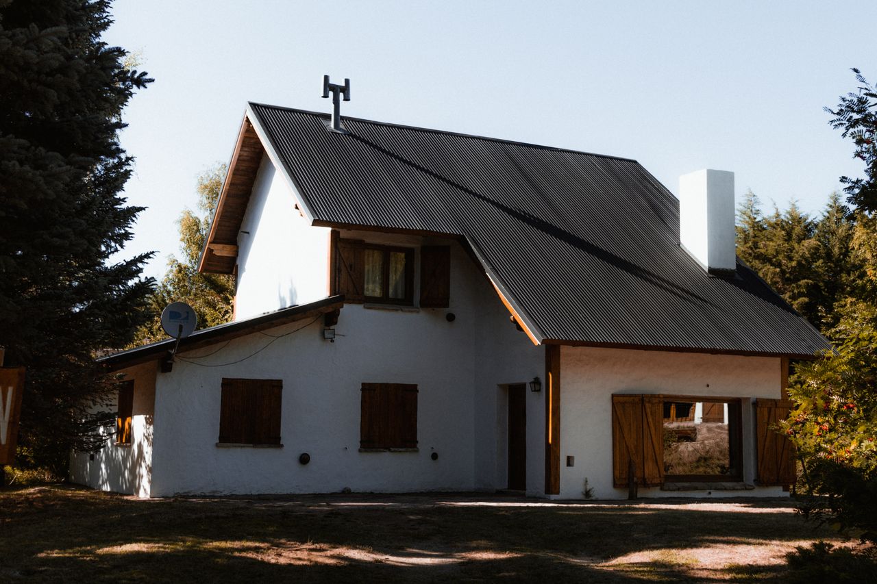A rustic country house with wooden shutters surrounded by lush greenery under daylight.
