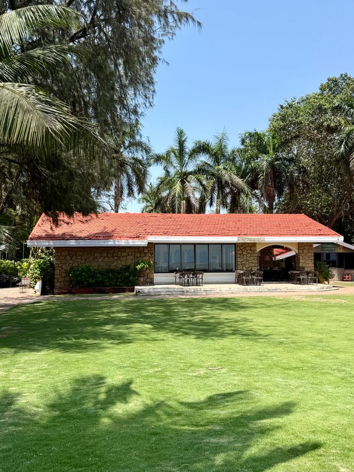 Cozy bungalow with a red roof surrounded by palm trees and green lawn.